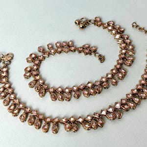 Op de afbeelding: Twee gouden enkelbandjes met roze kristallen versieringen. De enkelbandjes zijn gemaakt van een delicate ketting met hangende traanvormige kristallen.