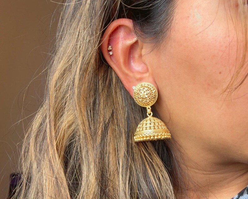 May include: Gold dangle earrings with a round, ornate design. The earrings have a smaller, round, ornate charm hanging from the larger charm.