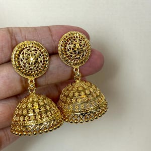 May include: A pair of gold-tone dangle earrings with intricate floral designs. The earrings feature a round top with a smaller, round, bell-shaped bottom.