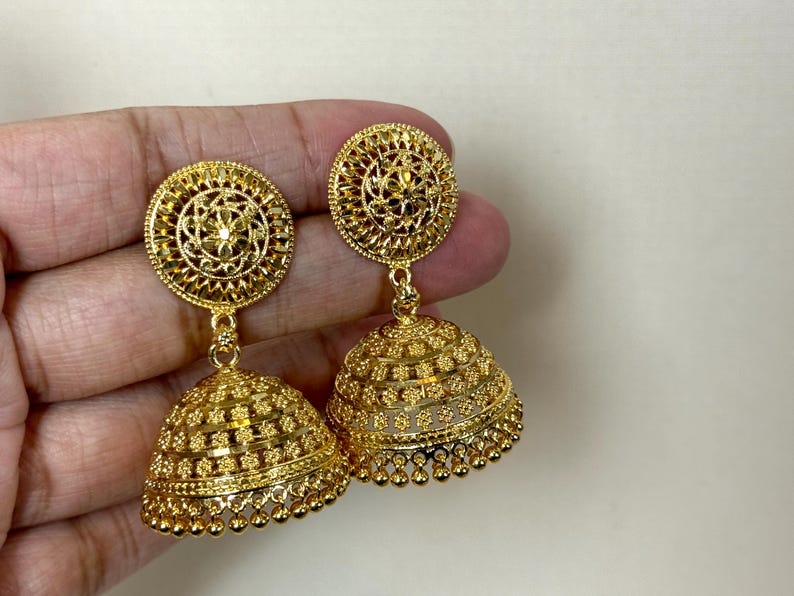 May include: A pair of gold-tone dangle earrings with intricate floral designs. The earrings feature a round top with a smaller, round, bell-shaped bottom.
