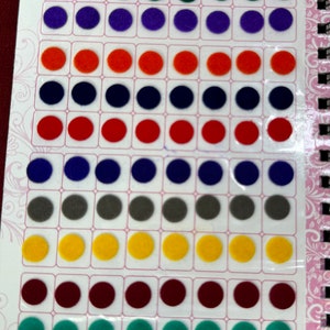 May include: A sheet of colourful felt dots, arranged in rows, for use as bindis. The sheet is labelled "Ananya Kumkum Bindi" and "Spiral Book".