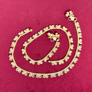 Op de afbeelding: Een paar gouden enkelbandjes met kleine, heldere steentjes. De enkelbandjes zijn op elkaar gelegd en hebben een delicaat ontwerp.