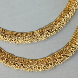 Op de afbeelding: Een paar gouden enkelbandjes met delicate parelversieringen. De enkelbandjes zijn gemaakt van een fijn gaasontwerp en hebben een franje van parels.