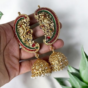 May include: A pair of gold-tone earrings with a peacock design and red and green accents. The earrings have a dangling bell-shaped charm.