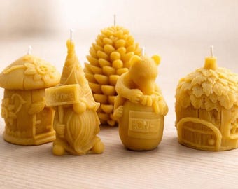 May include: Five yellow beeswax candles in various shapes: a mushroom house, a gnome holding a sign, a pinecone, a bear hugging a honey pot, and a house with a door. The candles are on a light brown wooden surface.
