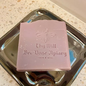 May include: A lavender-colored bar of soap with a bee and the text "Thy Will Bee-Done Apiary" embossed on the top.