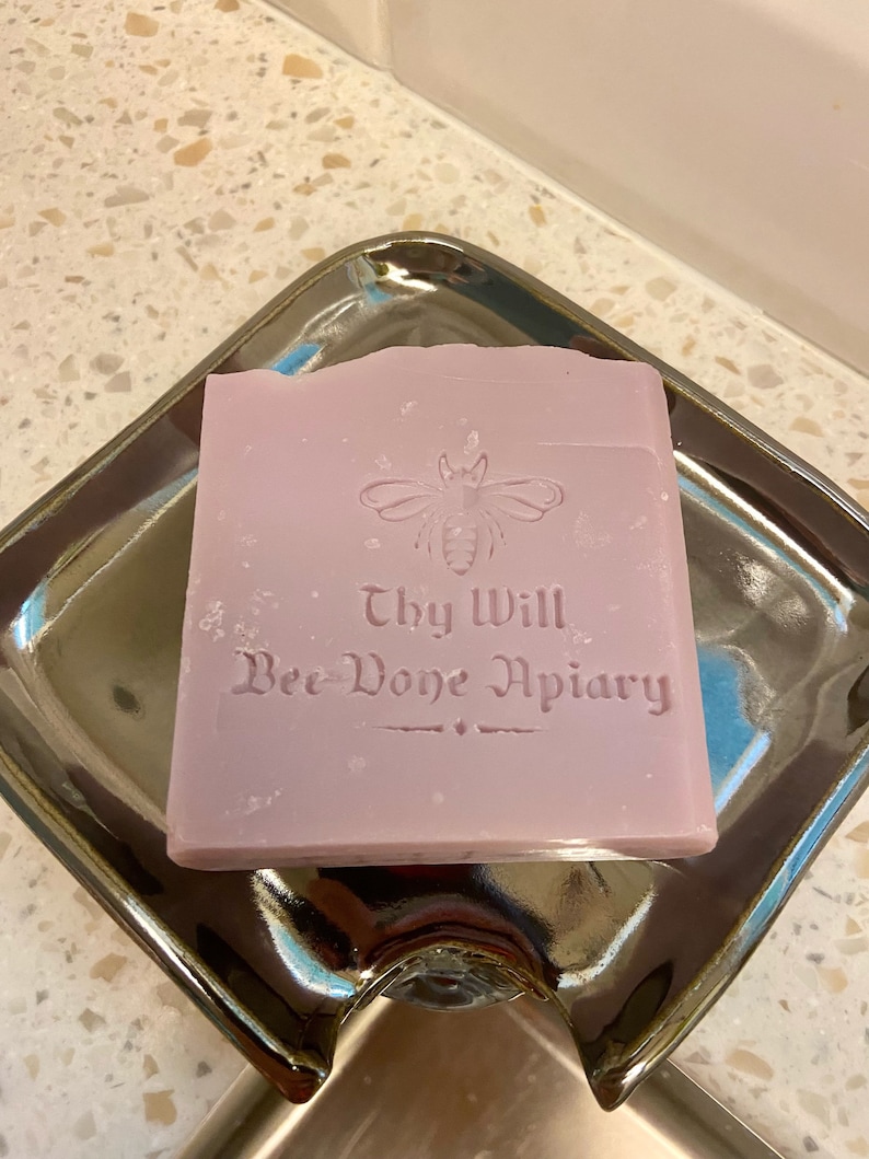 May include: A lavender-colored bar of soap with a bee and the text "Thy Will Bee-Done Apiary" embossed on the top.
