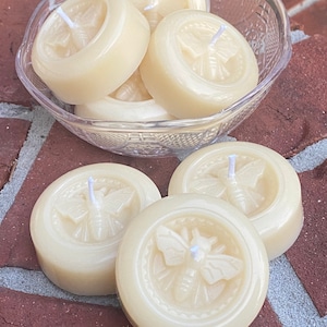 Peut inclure: Un ensemble de six bougies rondes de couleur blanc cassé avec un motif d'abeille en relief. Les bougies sont dans un bol en verre transparent.
