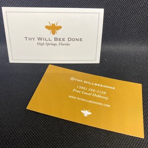 May include: Two business cards with a bee logo. One card is white with the text "THY WILL BEE DONE" and "High Springs, Florida." The other card is gold with contact information and a bee logo.