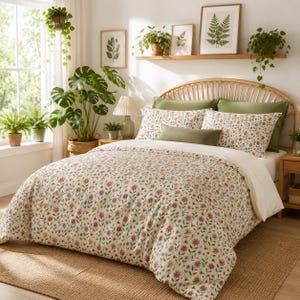May include: A bed featuring a duvet cover with a cream background and a multi-colored floral pattern, paired with matching pillowcases, a solid olive green bolster pillow, and a light-colored wooden headboard with a curved, slatted design.