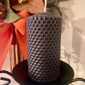 May include: A cylindrical charcoal gray pillar candle featuring a textured honeycomb pattern across its entire surface. The candle has a single white cotton wick centered at the top and is positioned upright on a black metal candle holder.