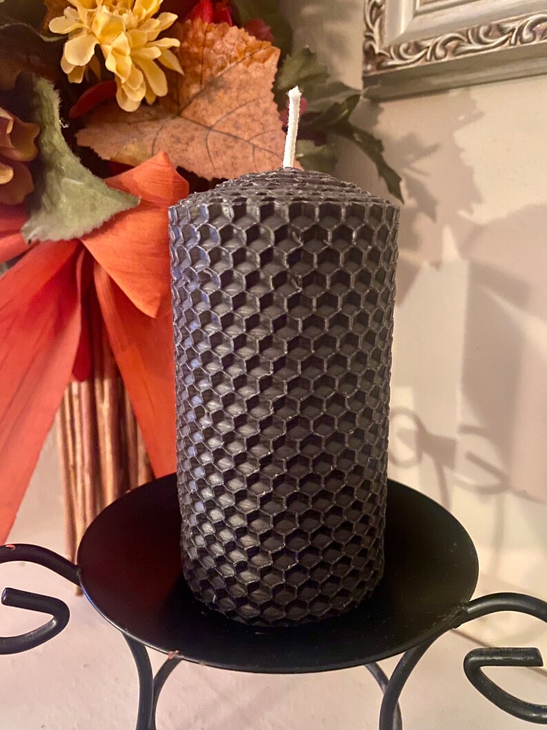 May include: A cylindrical charcoal gray pillar candle featuring a textured honeycomb pattern across its entire surface. The candle has a single white cotton wick centered at the top and is positioned upright on a black metal candle holder.