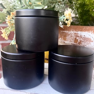 Pu&ograve; includere: Tre contenitori cilindrici con finitura nera opaca e coperchi abbinati. I contenitori sono disposti in una pila con uno posizionato sopra gli altri due, caratterizzati da un esterno liscio a tinta unita e un design semplice e uniforme.