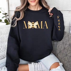 May include: Black sweatshirt featuring the word "MAMA" in gold, with a bee graphic replacing the "O". The sleeve has embroidered bees. A comfortable, casual style sweatshirt.