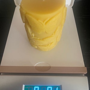 以下が含まれることがあります： 白い芯が付いた、円筒形の黄色の蜜蝋キャンドル。キャンドルは葉の模様で装飾されています。キャンドルの重さは0.41キログラム、257グラムで、デジタルスケールに表示されています。