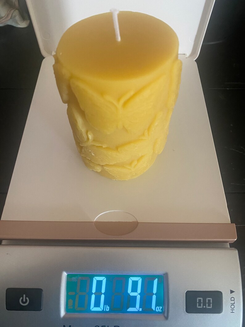 以下が含まれることがあります： 白い芯が付いた、円筒形の黄色の蜜蝋キャンドル。キャンドルは葉の模様で装飾されています。キャンドルの重さは0.41キログラム、257グラムで、デジタルスケールに表示されています。