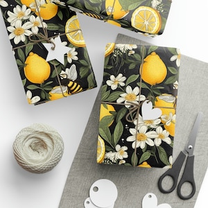 May include: Three gift boxes wrapped in black and white patterned paper with lemons, bees, and flowers. The paper has a dark background with white flowers, yellow lemons, and black bees.