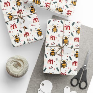 May include: Wrapped gifts with a white background, patterned with yellow and black bees, red gift boxes, and green sprigs. The gifts are tied with twine and have white star-shaped tags. A ball of twine, scissors, and blank tags are also present.
