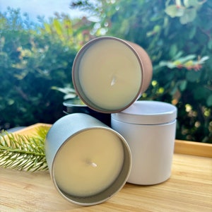 May include: Three cylindrical candles in metal tins, one silver, one white, and one copper-toned, each filled with smooth off-white wax and featuring a single centered cotton wick. The candles are arranged in a cluster, showcasing their metallic finishes.