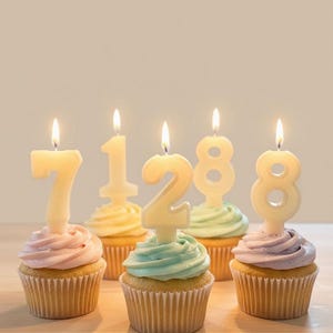 May include: Five cupcakes with pastel frosting and number-shaped candles that spell out "71288". The candles are lit, and the cupcakes are in paper liners. The cupcakes are on a light-colored surface.