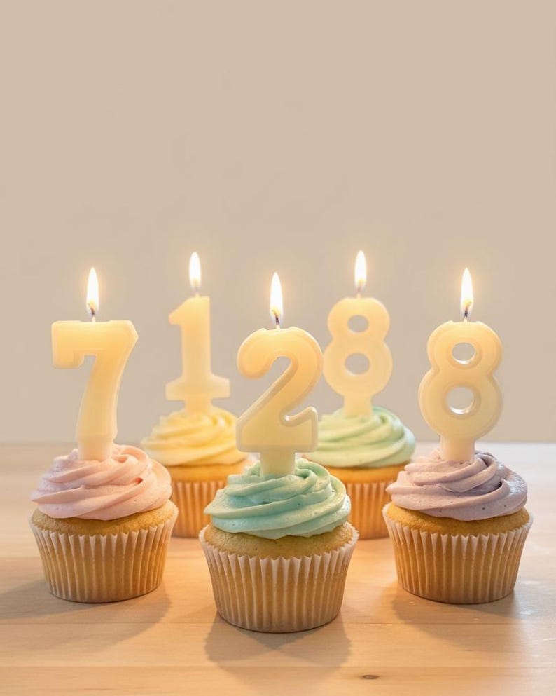 May include: Five cupcakes with pastel frosting and number-shaped candles that spell out "71288". The candles are lit, and the cupcakes are in paper liners. The cupcakes are on a light-colored surface.