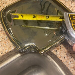 May include: A green ceramic dish with a chipped edge, measured with a yellow tape measure. The tape measure reads 4 inches.