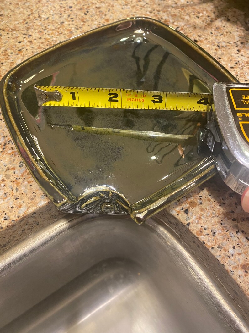 May include: A green ceramic dish with a chipped edge, measured with a yellow tape measure. The tape measure reads 4 inches.