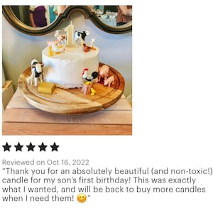 May include: A white frosted cake decorated with farm animal figurines and a number one candle. The cake sits on a wooden serving board. The cake is for a first birthday celebration.