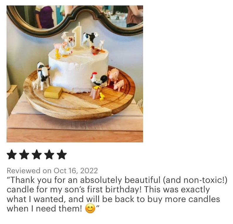 May include: A white frosted cake decorated with farm animal figurines and a number one candle. The cake sits on a wooden serving board. The cake is for a first birthday celebration.