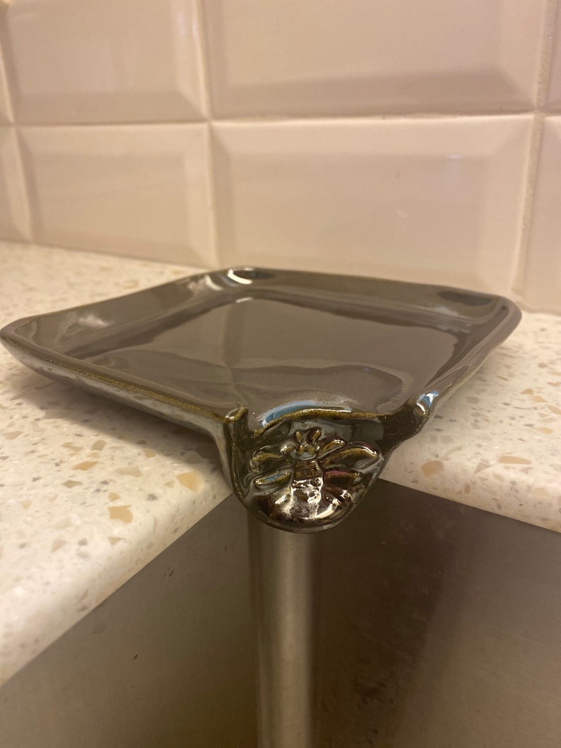 May include: A dark gray ceramic dish with a decorative bee design on the corner. The dish is sitting on a countertop.