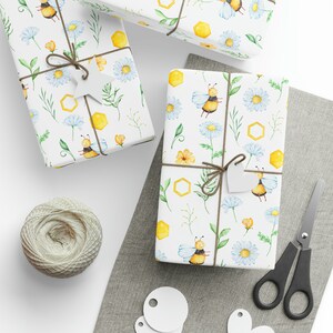 May include: Several gift-wrapped boxes with a bee and floral design on a white background. The presents are tied with twine and have white tags. A ball of twine, scissors, and blank tags are also visible, suggesting a crafting or gift-giving theme.