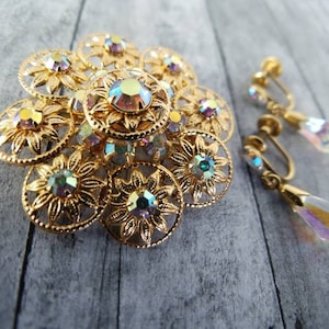 May include: A vintage gold-tone jewelry set featuring a floral brooch and matching clip-on earrings. The brooch has a layered design with iridescent crystal accents. The earrings have teardrop-shaped iridescent crystal pendants.