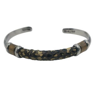 May include: A silver cuff bracelet with a central band of textured, dark brown and tan material. The bracelet has a curved, open design with silver ends and tan accents.