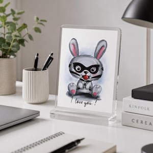 May include: A clear acrylic frame holding a print of a grey cartoon rabbit wearing a black leather mask and a red ball gag. The rabbit has pink inner ears and paws. The text "I love you!" is printed in black cursive script below the illustration.
