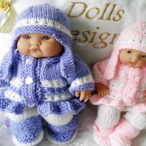 May include: Two knitted doll outfits, one in purple and white and the other in pink and white. Both outfits include a hat, jacket, and trousers. The dolls are not included in the image.