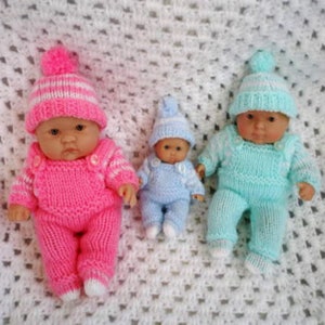 Könnte beinhalten: Drei gestrickte Puppenoutfits in Pink, Blau und Türkis. Jedes Outfit beinhaltet eine Mütze und einen Einteiler. Die Puppen sind nicht im Lieferumfang enthalten.