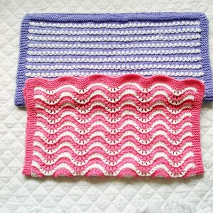 May include: Two knitted baby blankets, one in a light purple and white striped pattern and the other in a pink and white wavy pattern.
