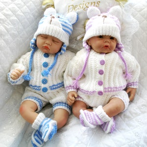 May include: Two knitted baby doll outfits, one in white with blue stripes and the other in white with purple stripes. Both outfits include a hat, cardigan, and trousers.