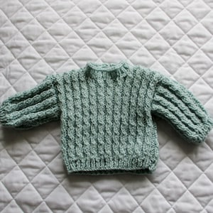 May include: A light green knitted baby sweater with a cable knit pattern.