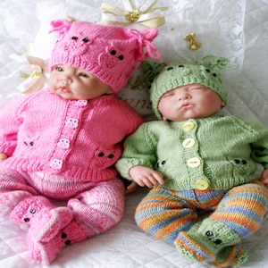 May include: Two baby dolls in handmade knitted outfits. One doll is in pink, the other in green. Each outfit includes a hat, cardigan, trousers, and booties, all with owl-shaped details. The outfits are hand-knitted, with a focus on detail.