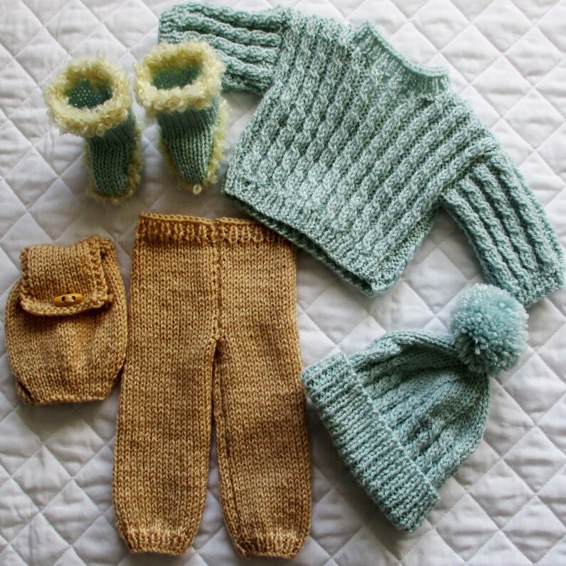 May include: A set of knitted baby clothes in blue and brown. The set includes a sweater, pants, a hat, and booties. The sweater has a cable knit pattern and the hat has a pom-pom on top.