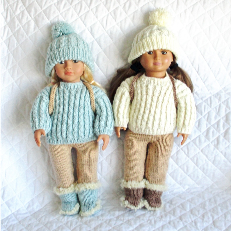 May include: Two dolls wearing knitted winter outfits. The doll on the left is wearing a light blue sweater, tan pants, and blue boots. The doll on the right is wearing a cream sweater, tan pants, and brown boots. Both dolls are wearing knitted hats with pom-poms.