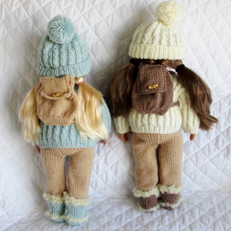 May include: Two knitted doll outfits with matching hats and backpacks. One outfit is light blue with a brown backpack, the other is white with a brown backpack.
