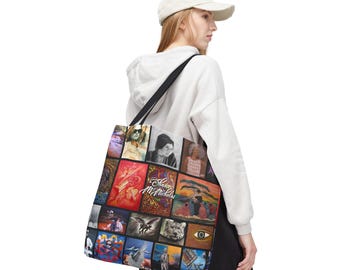 May include: A black tote bag featuring a collage of colorful images, including portraits and artwork. The bag has a black shoulder strap and is carried by a person wearing a white hoodie and a baseball cap.