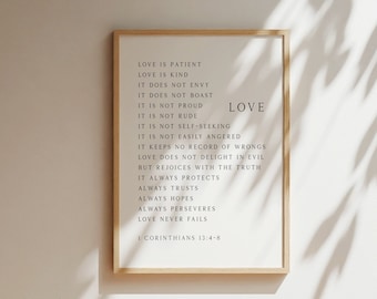 May include: A rectangular wall art print in a light wood frame featuring the text of 1 Corinthians 13:4-8. The white background displays black serif typography listing the attributes of love, with the word LOVE prominently placed on the right side.