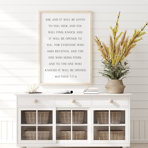 K&ouml;nnte beinhalten: Ein rechteckiges Wandschild in einem hellen Holzrahmen mit schwarzem Text: ASK AND IT WILL BE GIVEN TO YOU: SEEK AND YOU WILL FIND; KNOCK AND IT WILL BE OPENED TO YOU. FOR EVERYONE WHO ASKS RECEIVES. AND THE ONE WHO SEEKS FINDS. MATTHEW 7:7-8