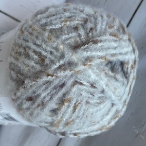 May include: A ball of white yarn with brown and gold flecks. The yarn is soft and fluffy, and it is perfect for knitting or crocheting.