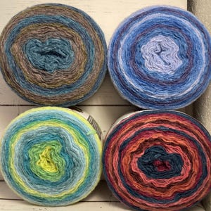 May include: Four skeins of yarn in various colors are arranged in a square. The yarn colors include shades of blue, green, yellow, pink, and brown. The yarn is wound in a circular pattern, with the center of each skein visible.