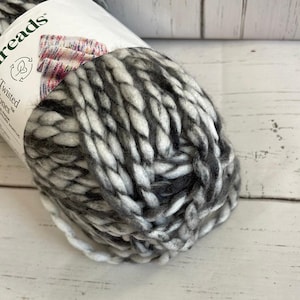 May include: Close-up of a ball of Twisted Tones yarn in grey and white. The yarn is thick and chunky, with a textured appearance. The label shows a sample of the yarn's colour variations and the brand name.