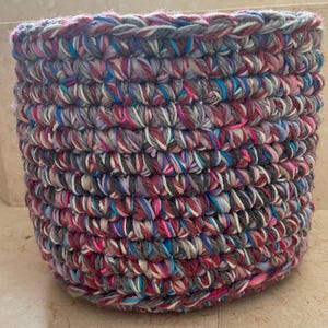 May include: A crocheted basket with a colorful, multi-colored yarn in shades of pink, blue, gray, and white.
